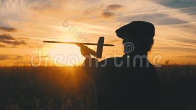 可爱的孩子在日落时在田里玩玩具木飞机。 小孩玩木飞机的剪影